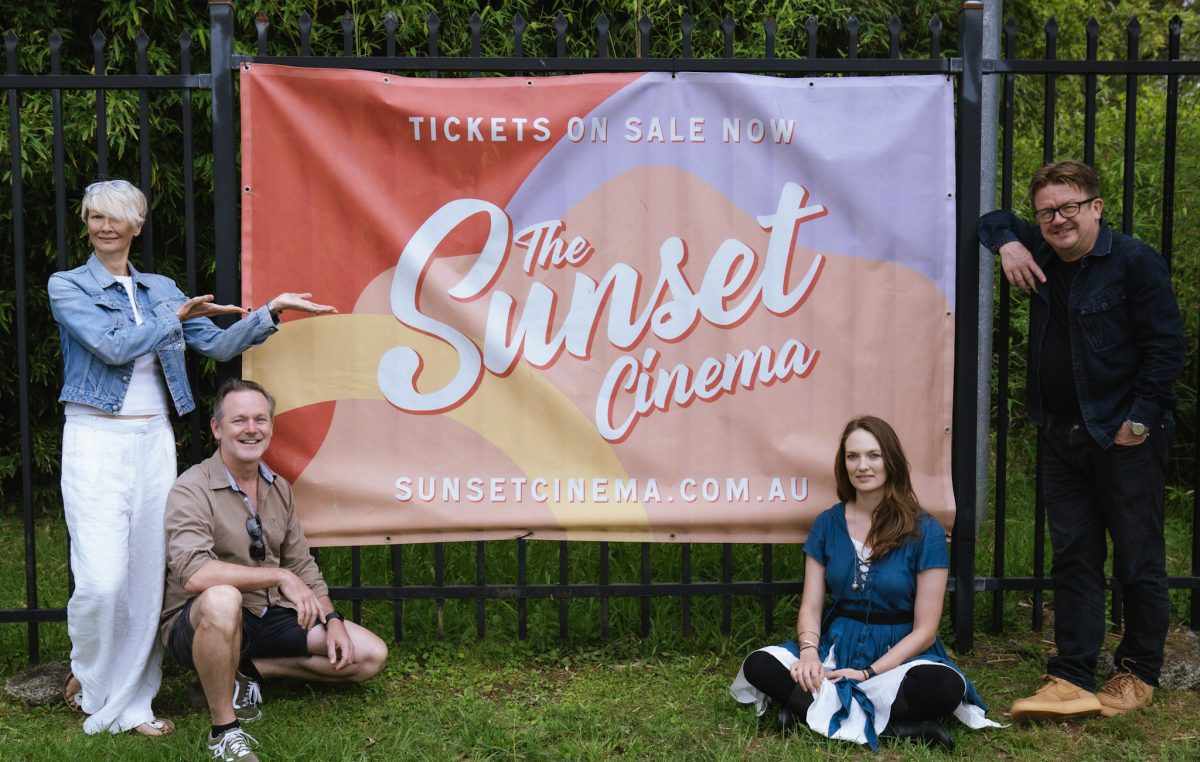 Two women and two men are gathered around a banner advertising the Wollongong Botanic Garden's Sunset Cinema.